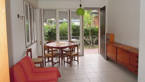 A dining area with a round table and chairs, a sofa, and a green pendant light. - Nice Flat With Garden and Parking (San Michele al Tagliamento)