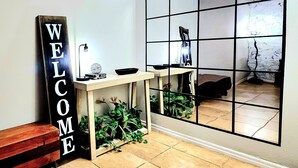 En modern inredning med en skylt som säger ”VÄLKOMMEN”, ett konsolbord med dekorativa föremål och ett stort fönster med utsikt.
