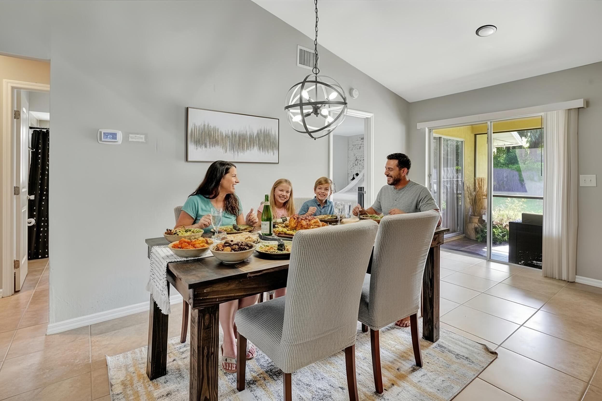 A family dining in a modern kitchen with a large dining table, chairs, and a chandelier.