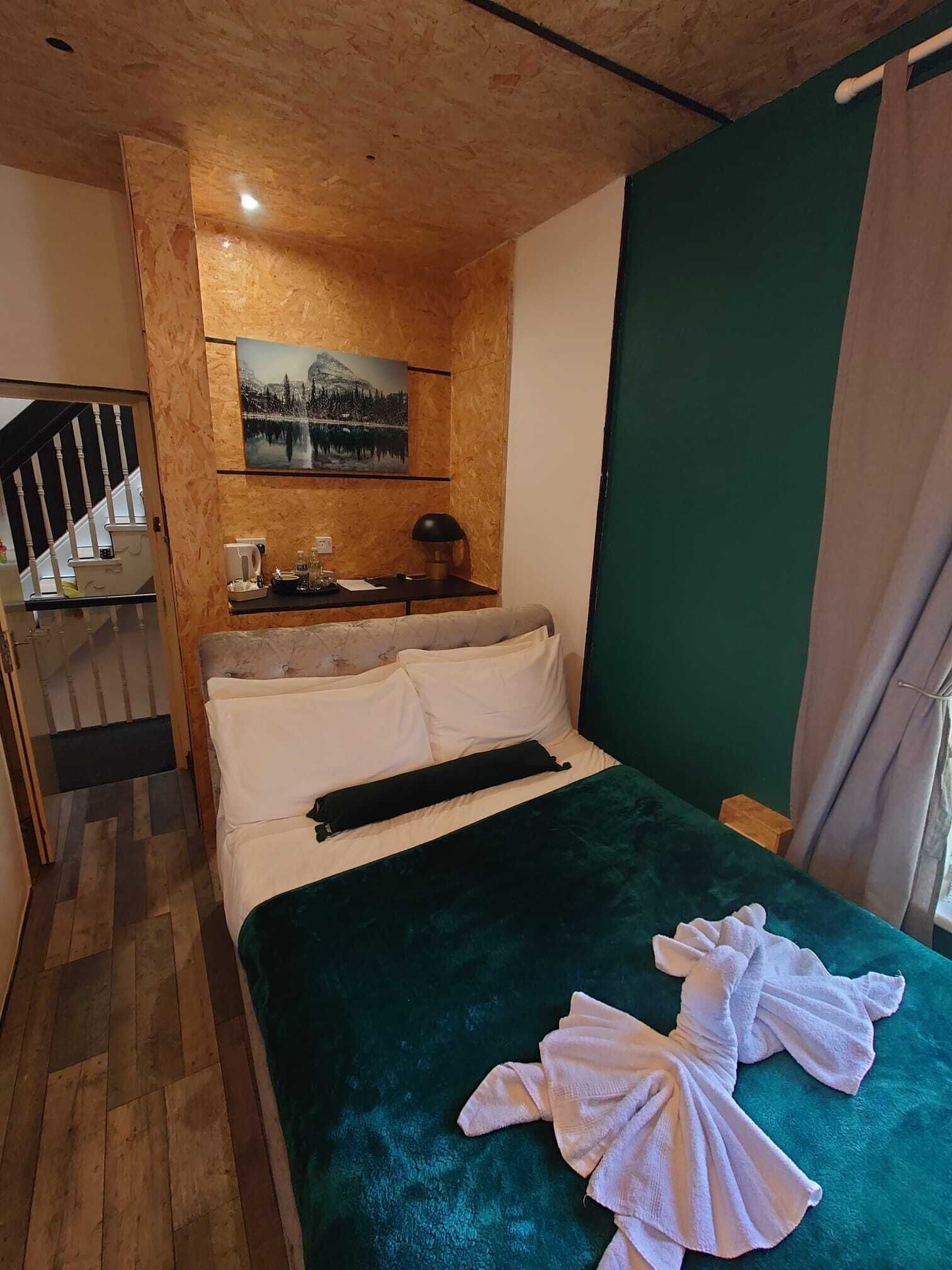 Habitación de hotel con cama, un cuadro en la pared, escritorio con lámpara y vistas a una escalera.