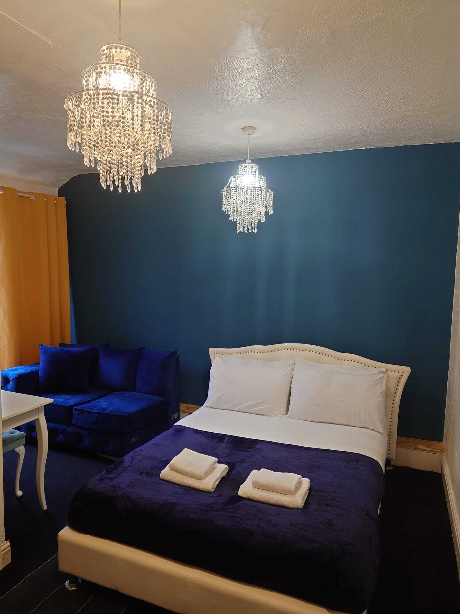 Un dormitorio con una cama, dos sofás azules, una mesa blanca y dos lámparas de araña.