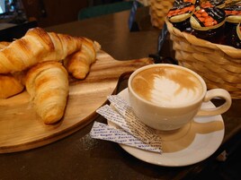 Een croissant, een koffiekopje met latte-art en een mandje jam op een houten tafel.