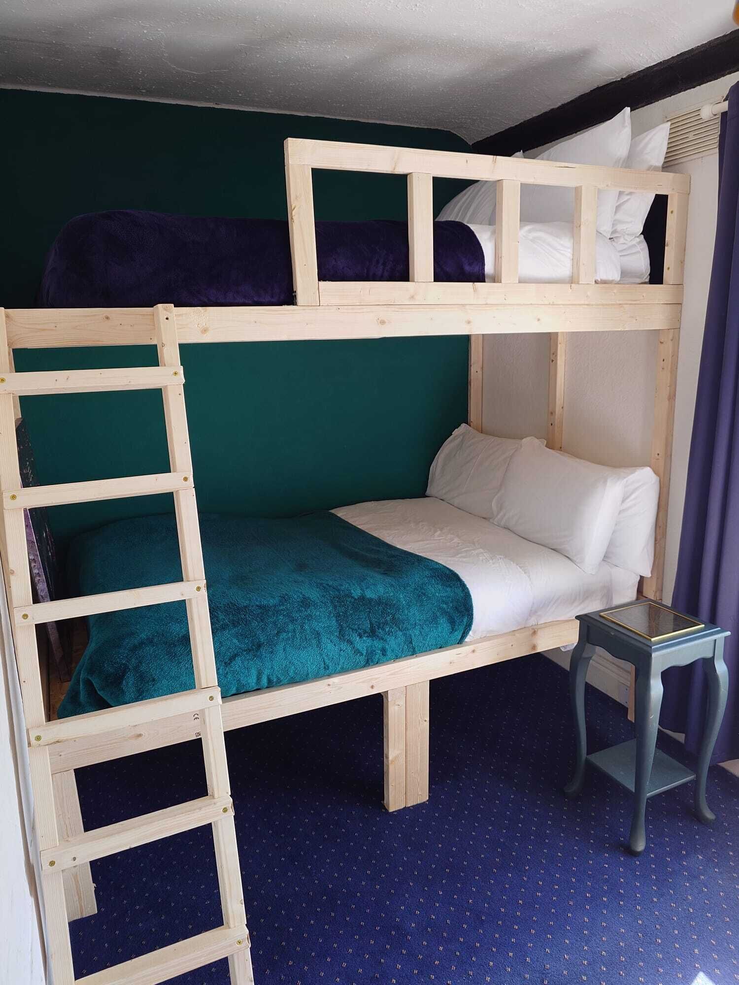 A bunk bed with a ladder, a small table, and a blue carpeted floor.