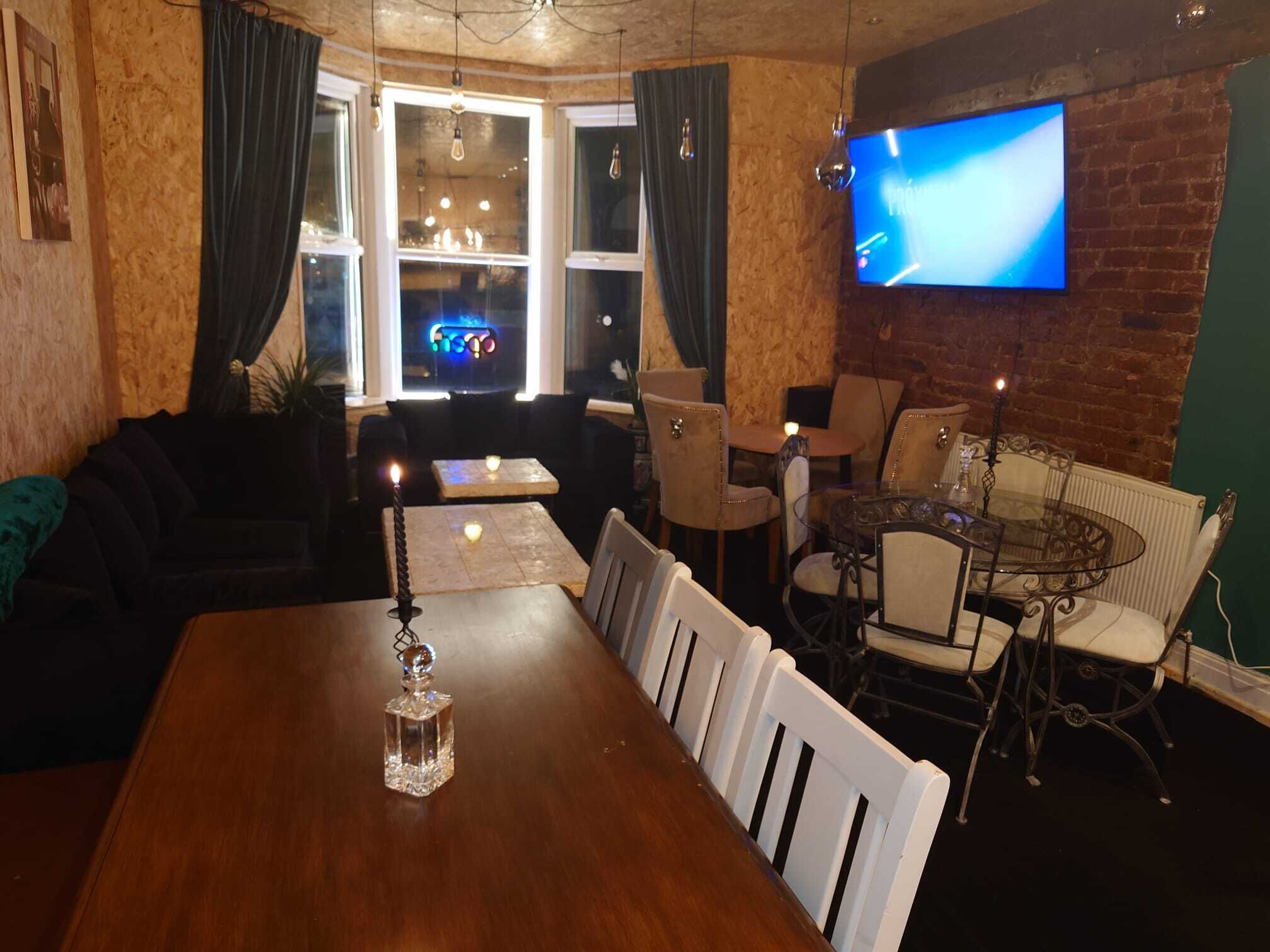 A cozy dining area with a wooden table, white chairs, and a TV mounted on a brick wall.
