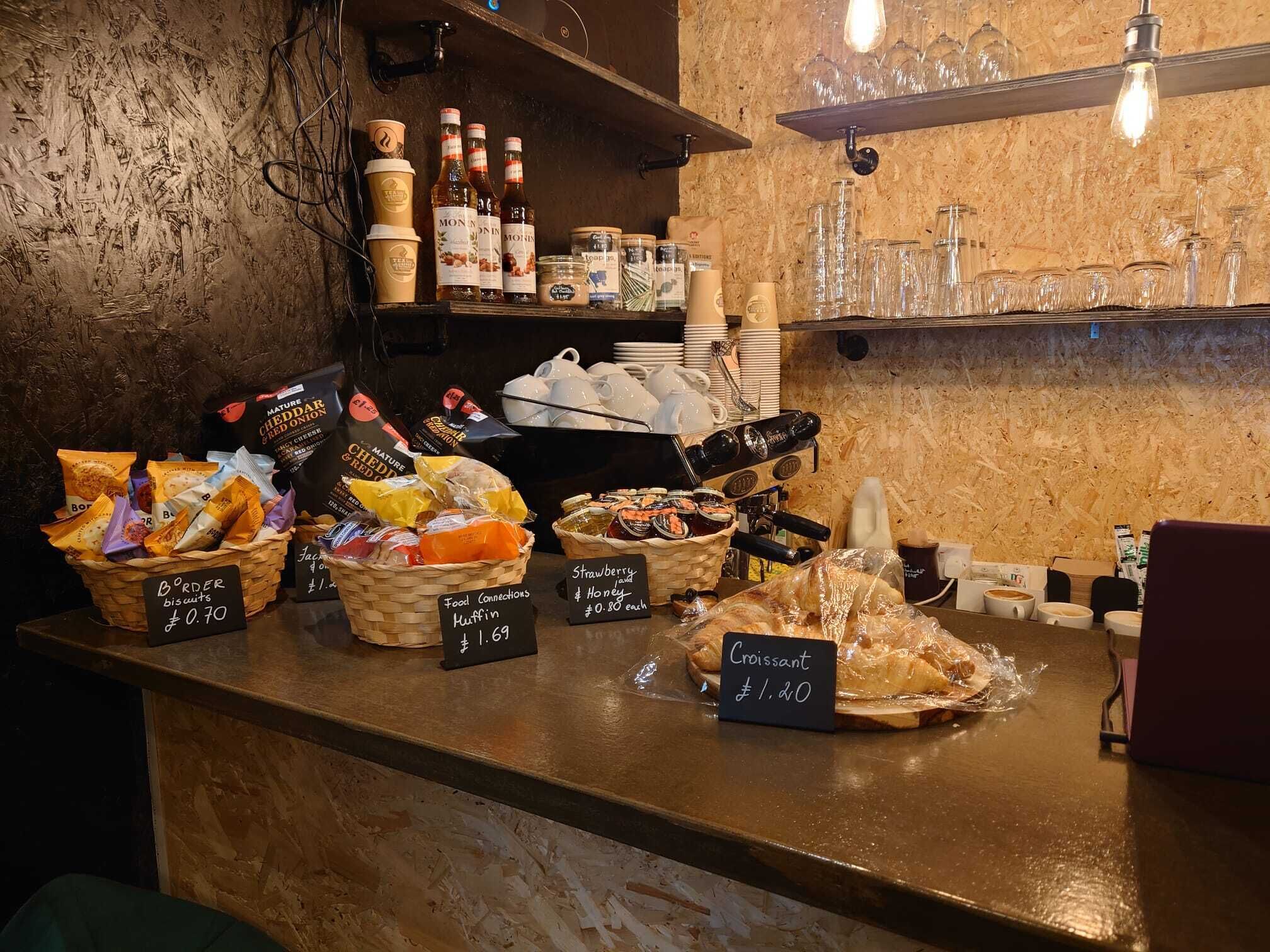A bakery counter with various baked goods and snacks, including muffins and croissants, priced at £1.69 and £1.20 respectively.