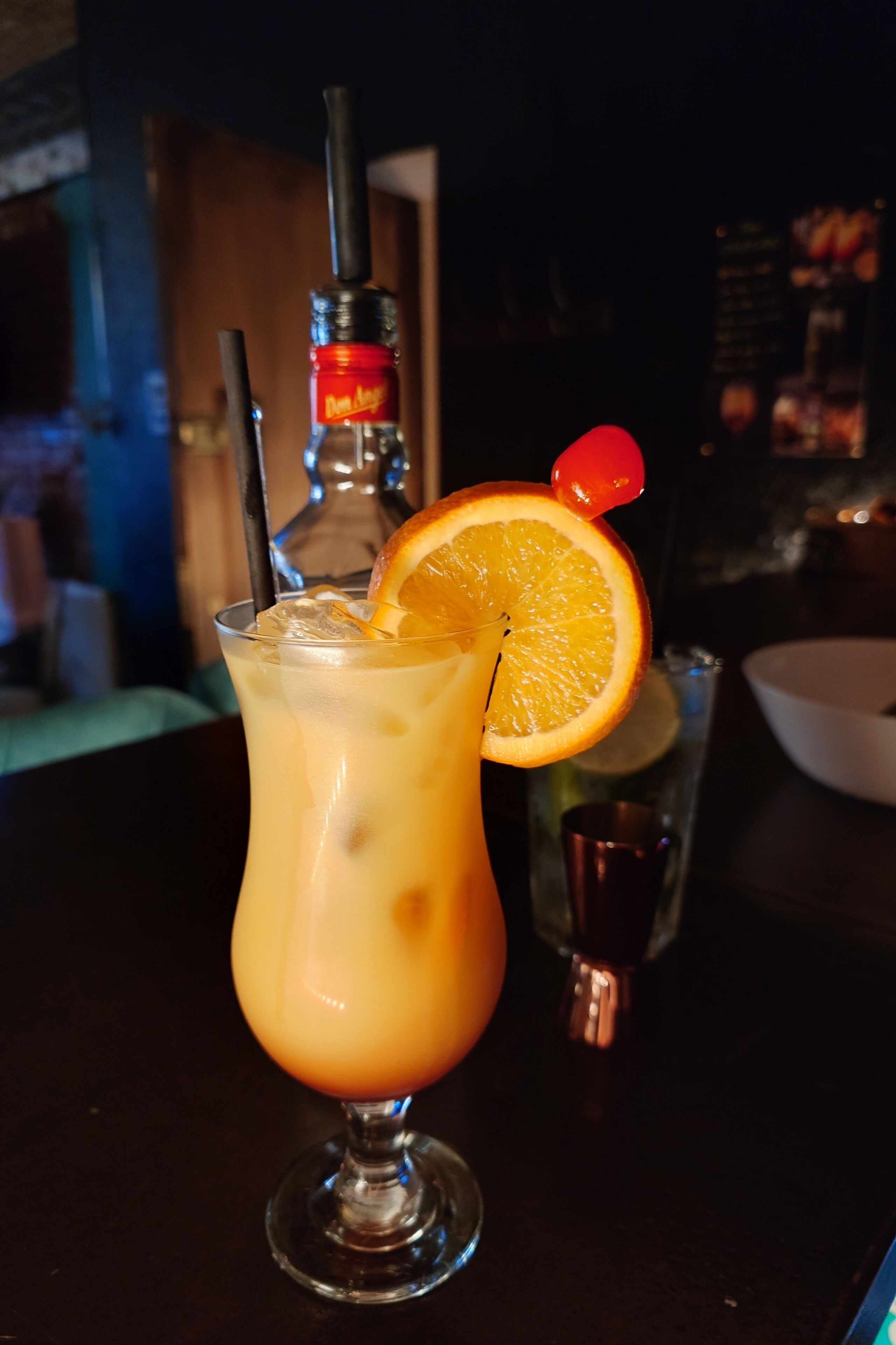 A cocktail with an orange slice garnish on a bar counter.