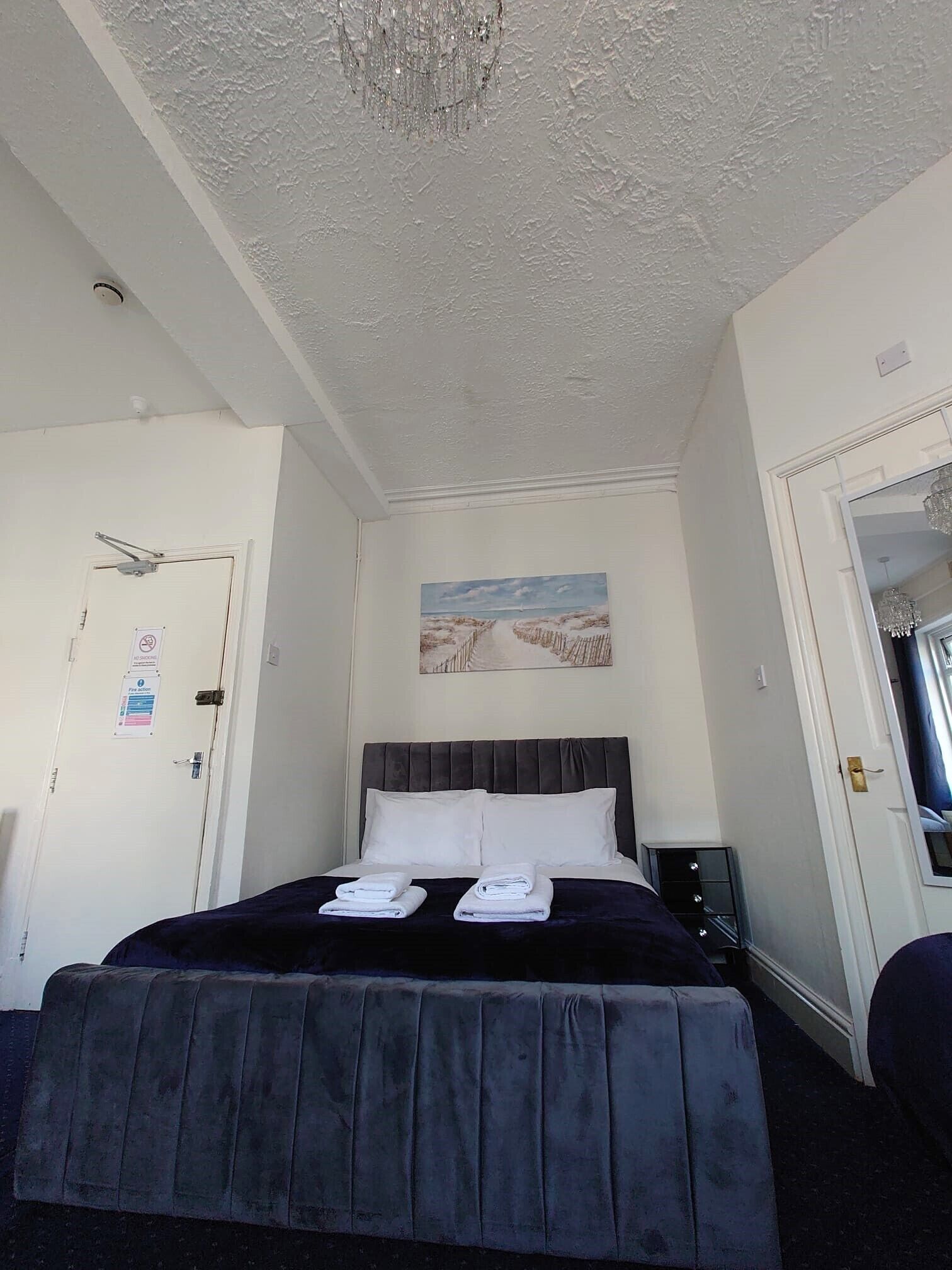 Een slaapkamer met een bed, een schilderij, een kroonluchter en een deur met een bordje.