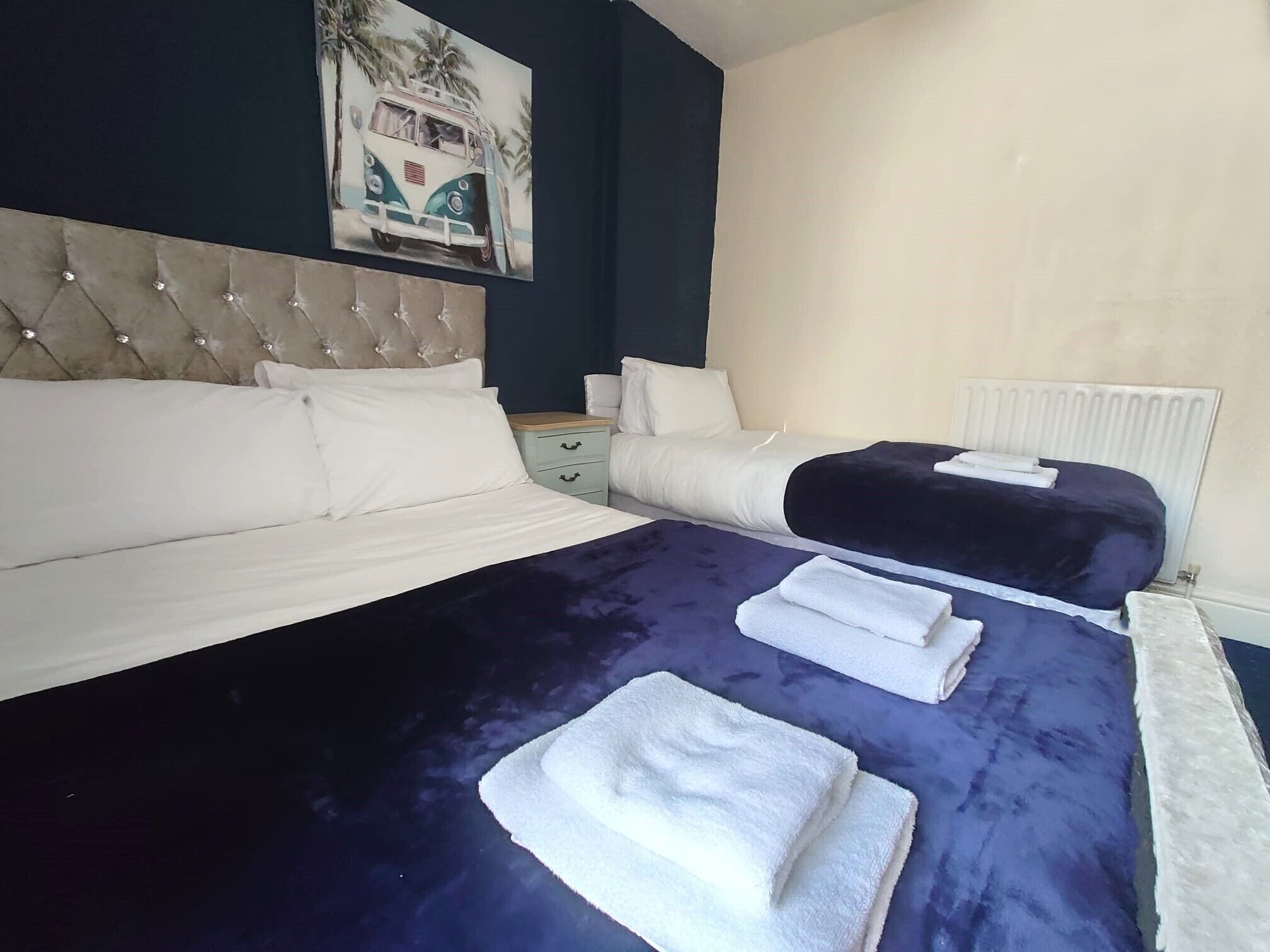 Une chambre d’hôtel avec un grand lit, un lit plus petit, une table de chevet, une commode et un radiateur.