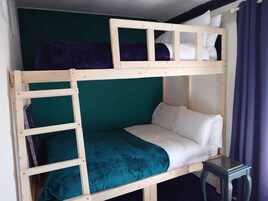 Een stapelbed met een ladder, een enkel bed beneden en een kleine tafel ernaast.