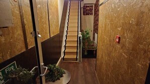 A narrow hallway with a wooden floor, a staircase with a light fixture above, and a small table with plants. - Harriette's Guest House (Blackpool)