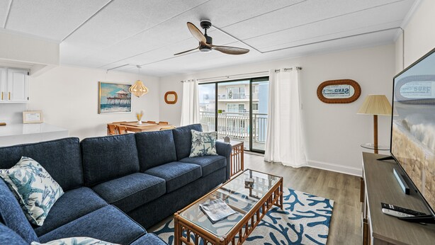 A modern living room with a blue sofa, glass coffee table, and a ceiling fan. - Newly remodeled with ocean views! Steps to the beach in the heart of midtown OC! (Ocean City)