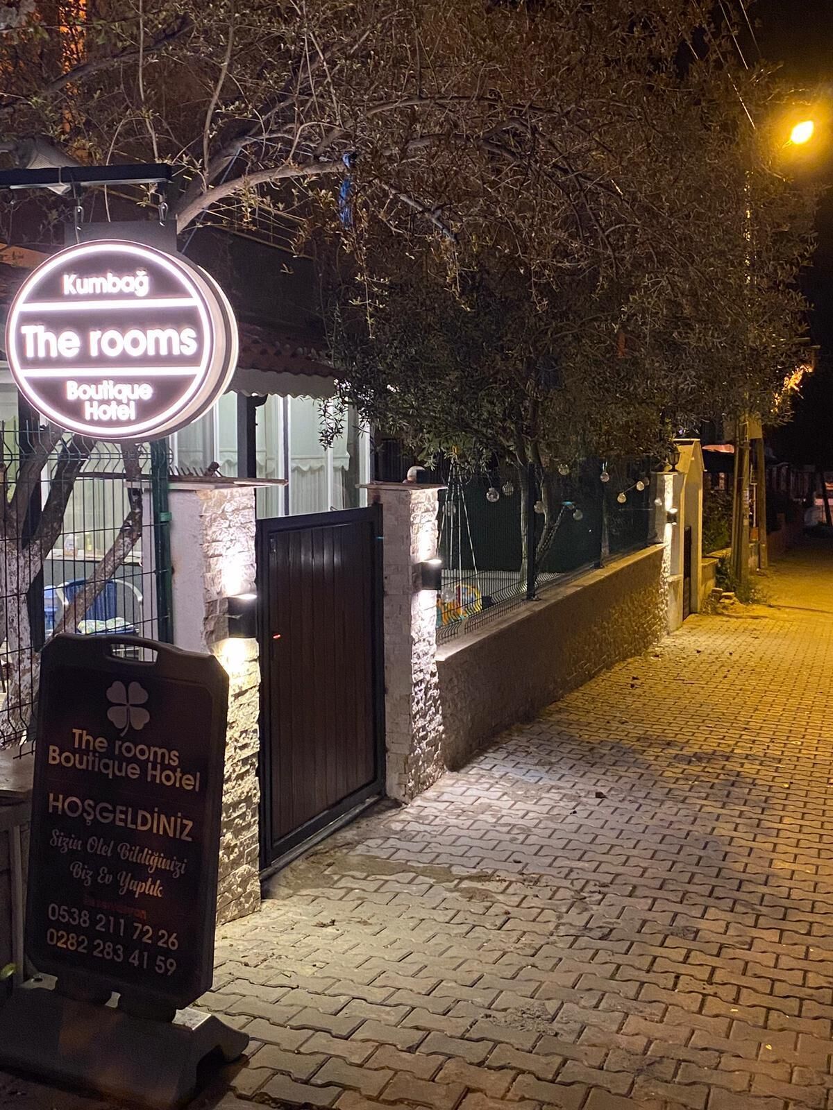 Señalización para 'The rooms Boutique Hotel' con números de contacto y un símbolo de trébol.