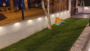 Un'area esterna ben illuminata con altalene, prato curato e recinzione.