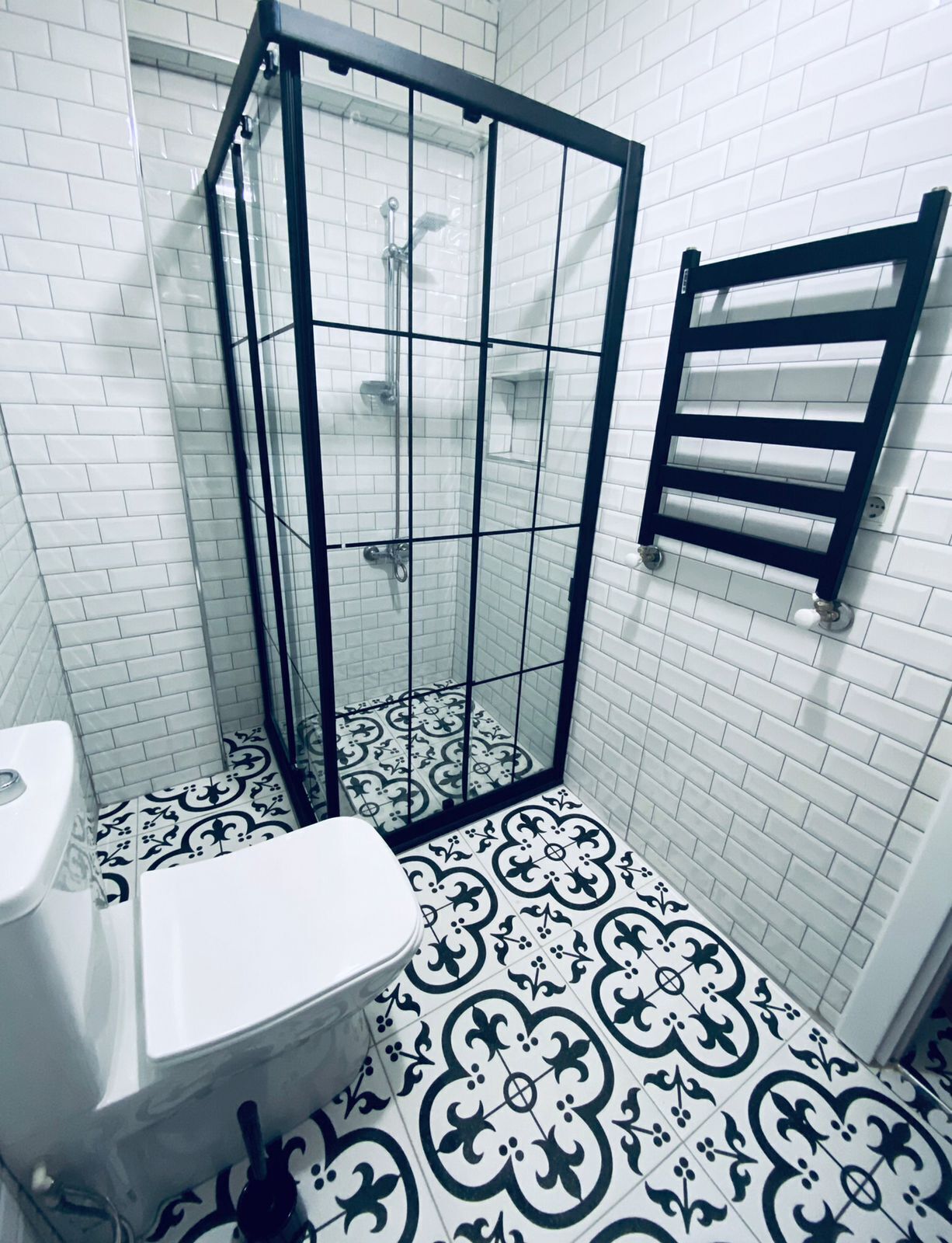 Une salle de bain avec une douche à parois de verre, des toilettes et des carreaux de sol à motifs.