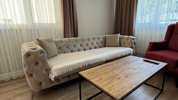 Ein Wohnzimmer mit einem beigen Sofa, einem Holztisch und einem roten Sessel.