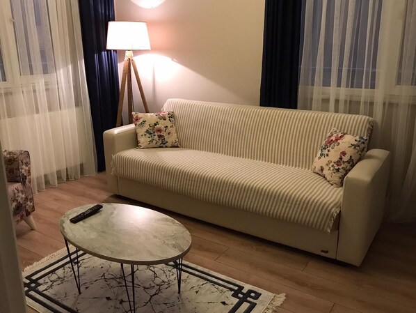 A living room with a sofa, a small round table, a lamp, and a floral-patterned chair.