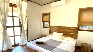 Een slaapkamer met een houten bed, een plafondventilator, een raam met gordijnen en een wandairconditioner.