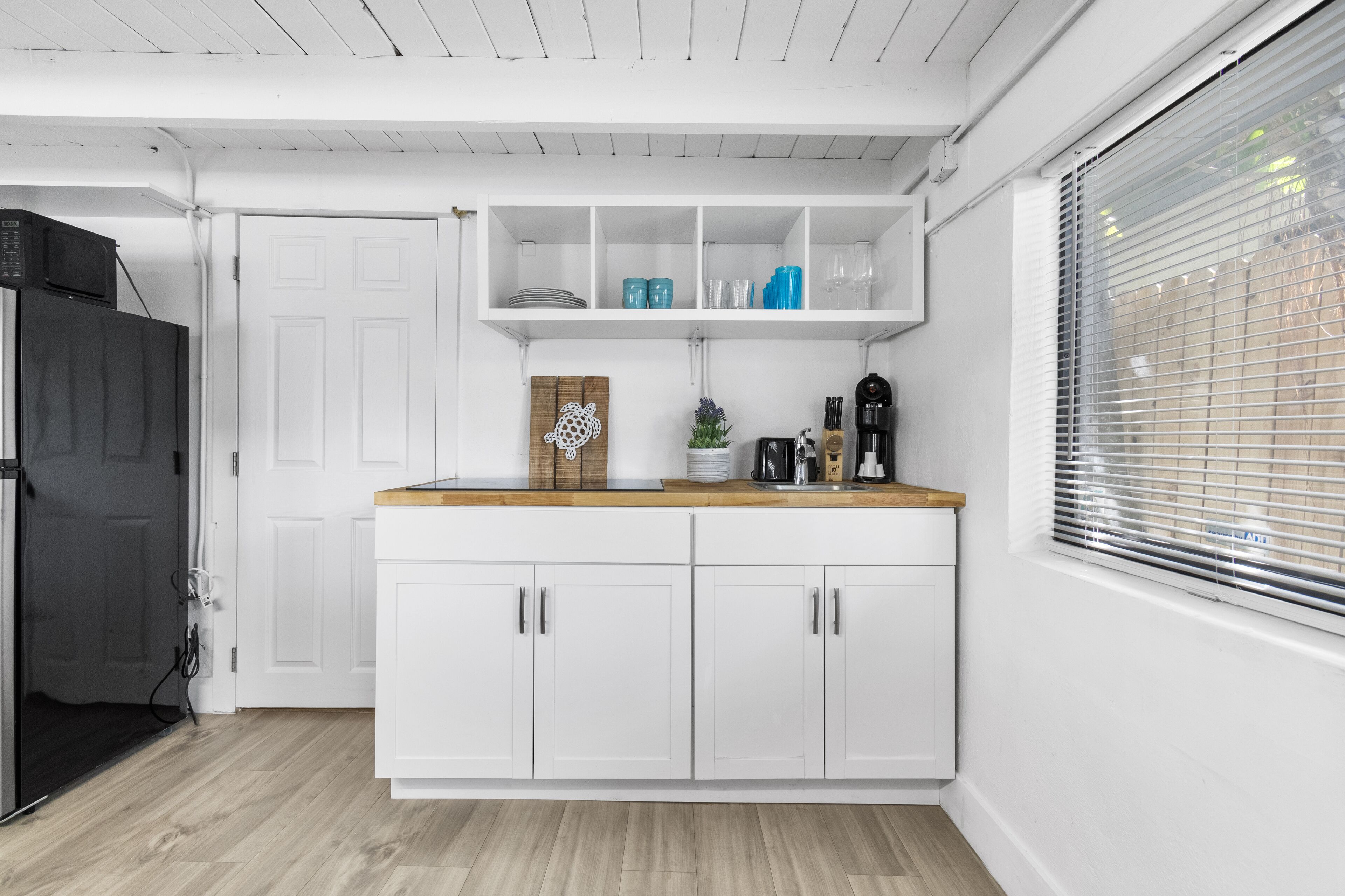 A modern kitchen with white cabinetry, a wooden countertop, and a built-in shelf above the sink.