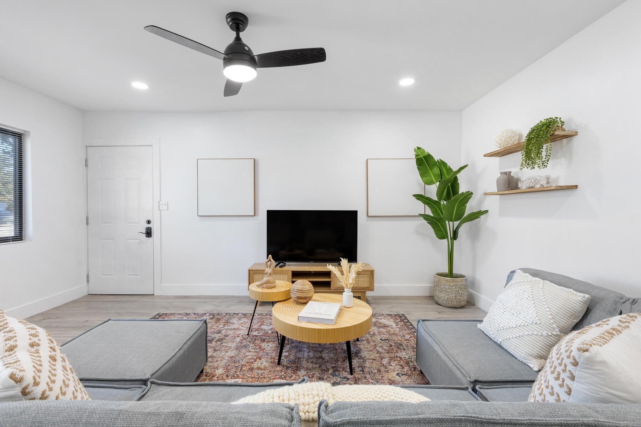 Una sala moderna con televisor de pantalla plana, ventilador de techo y una planta grande.