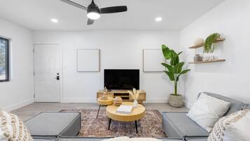 Una sala moderna con televisor de pantalla plana, ventilador de techo y una planta grande.