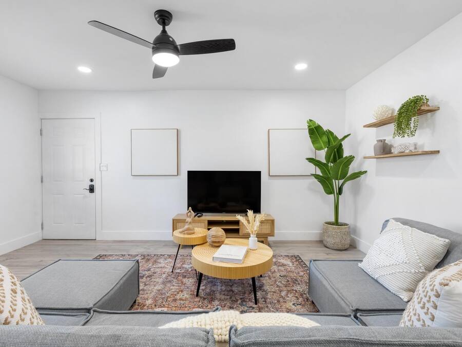 Una sala moderna con televisor de pantalla plana, ventilador de techo y una planta grande.