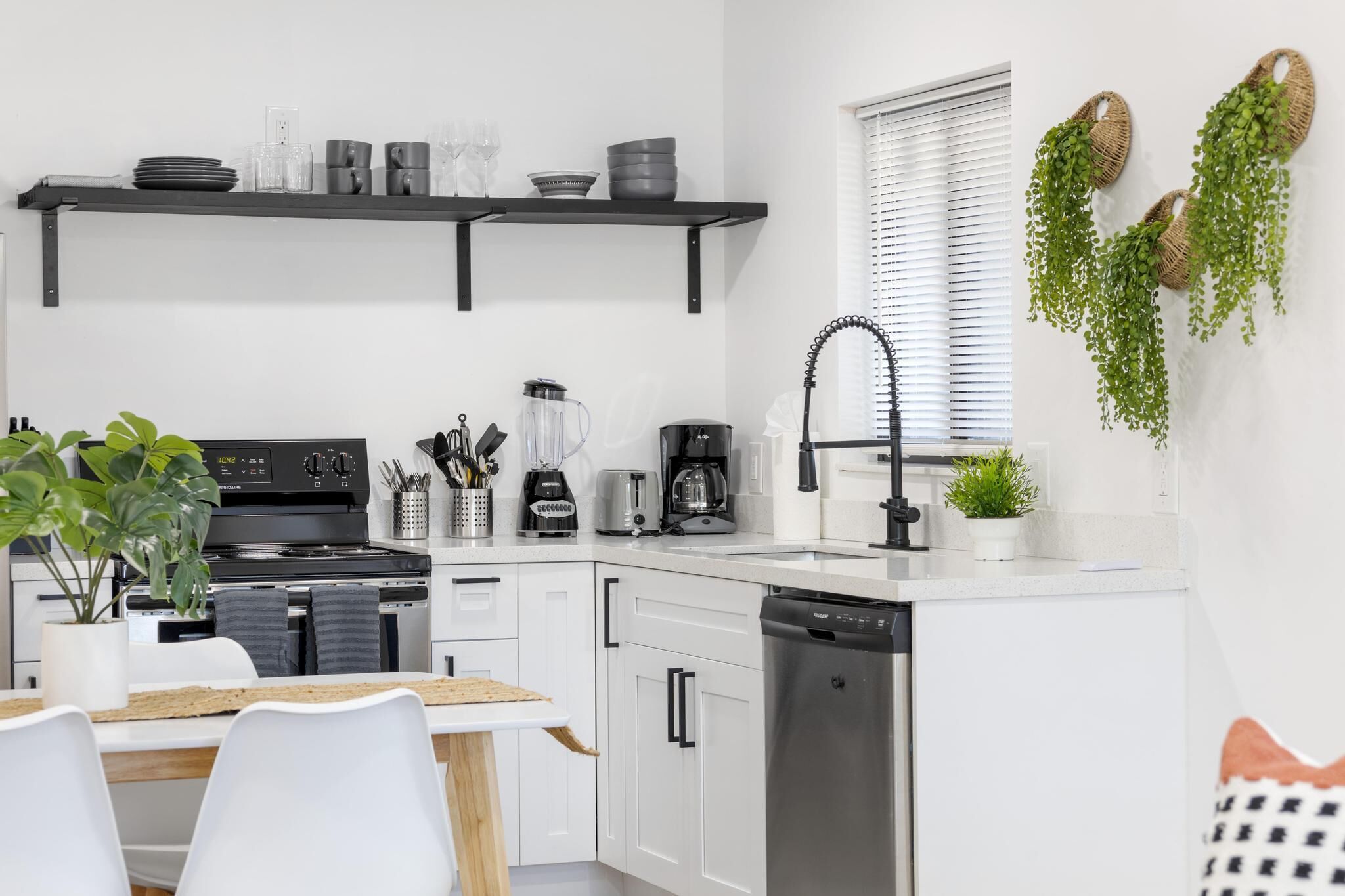 A modern kitchen with white cabinets, black appliances, and a dining area with a white table and chairs.