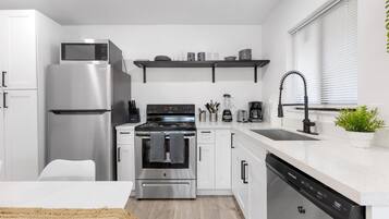 Una cocina moderna con electrodomésticos de acero inoxidable, armarios blancos y lavavajillas integrado.