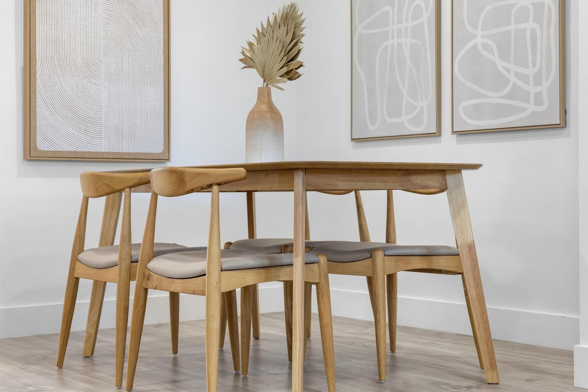 A wooden table with two chairs, a vase with dried plants, and abstract art on the wall.