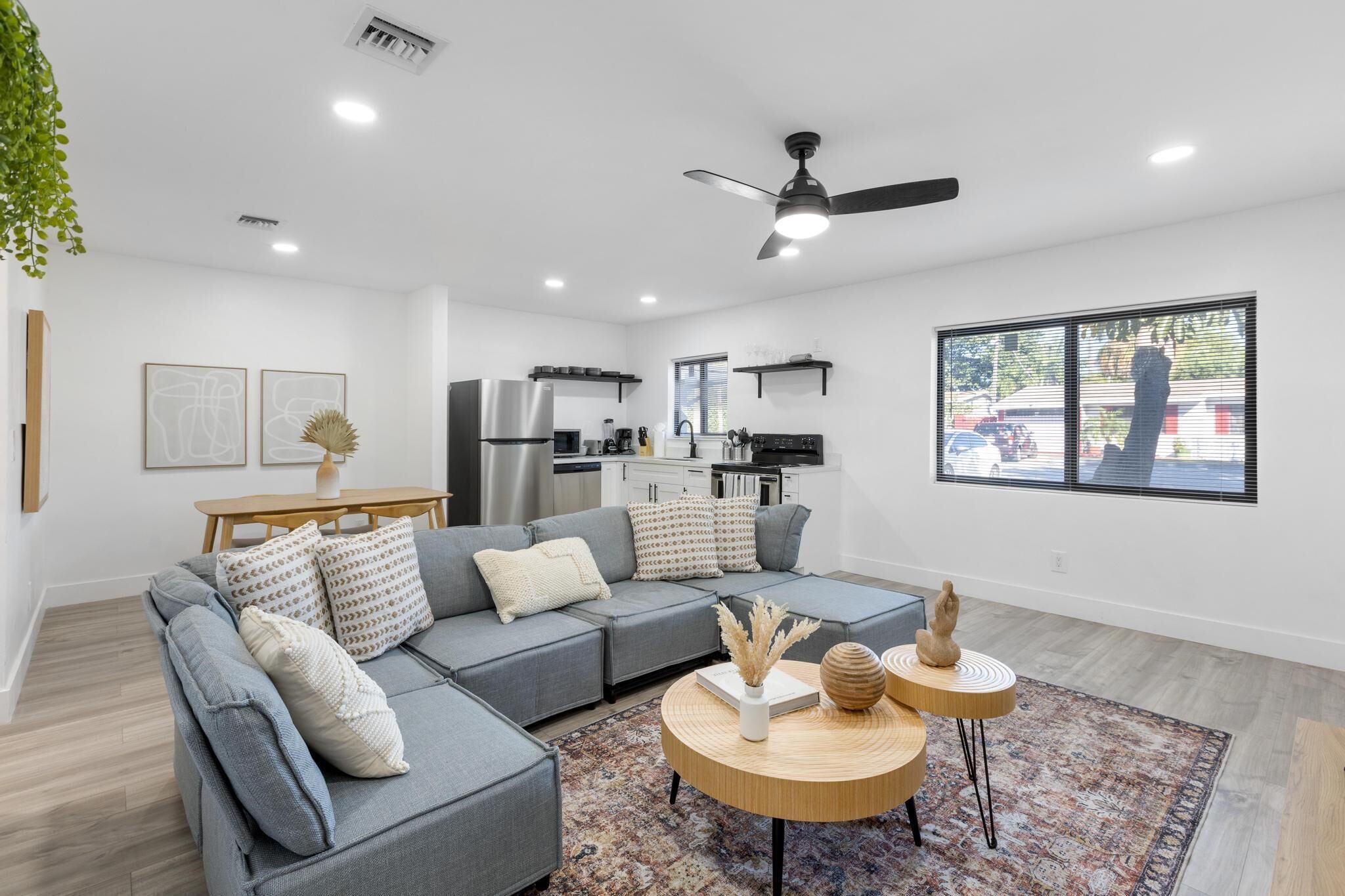 A modern living room with a grey sectional sofa, a round wooden coffee table, and a view of the kitchen in the background.