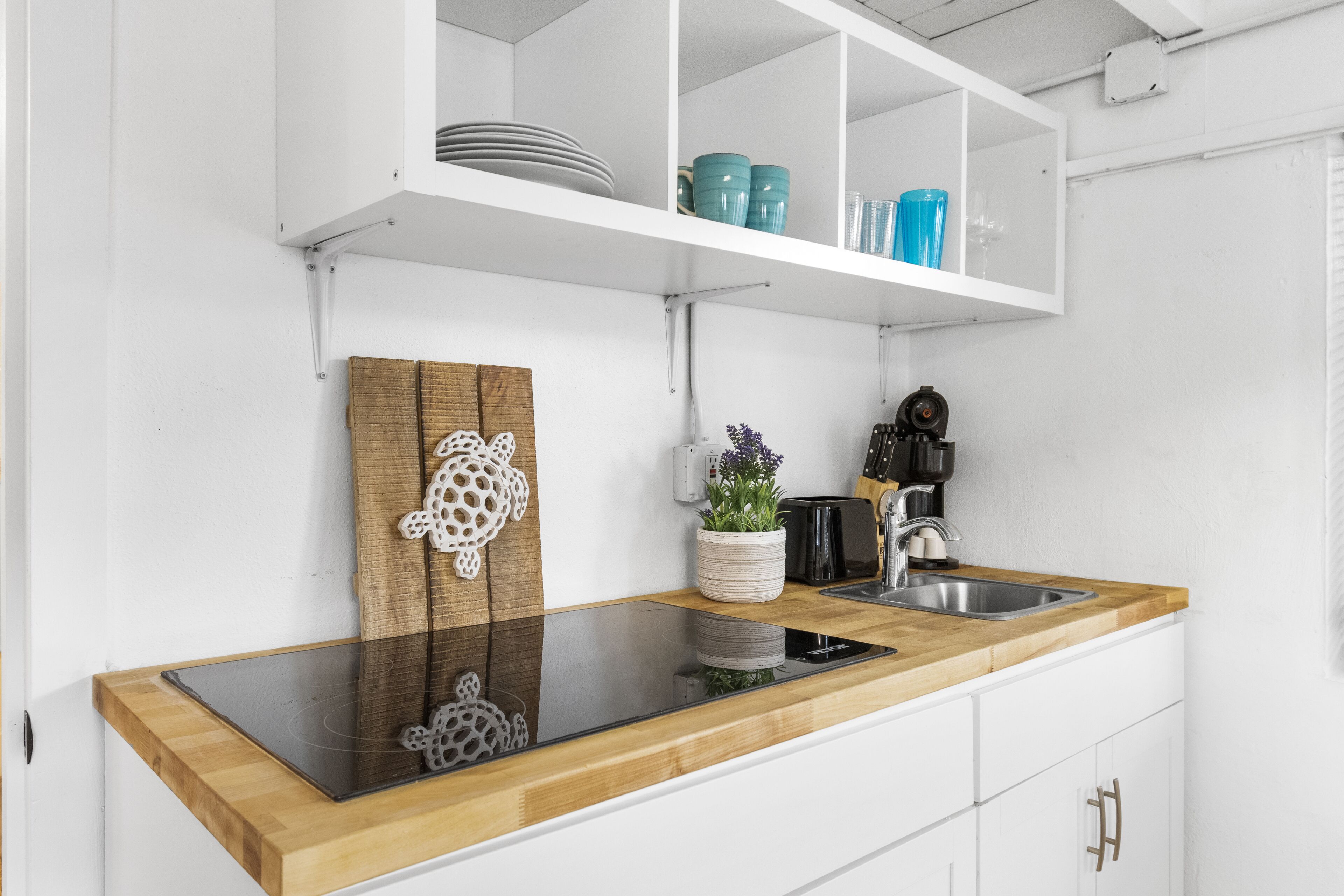 A modern kitchen with a wooden countertop, stainless steel sink, and white cabinetry.