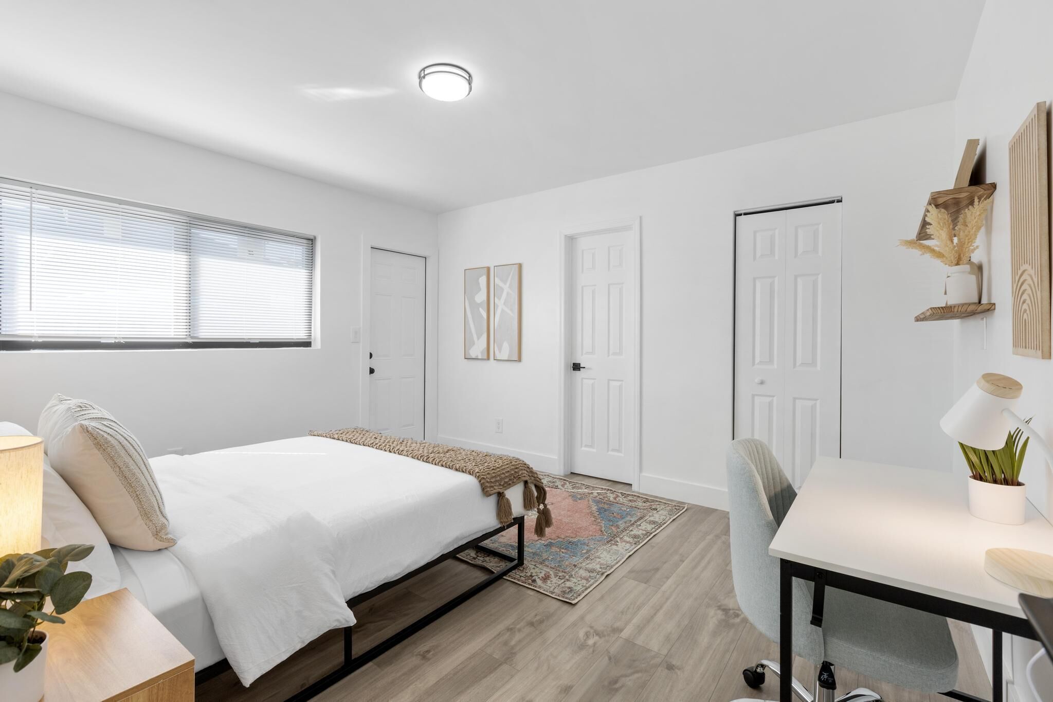 Quarto moderno com cama, mesa de cabeceira, abajur e escrivaninha com cadeira.
