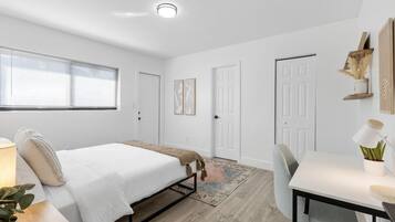 Quarto moderno com cama, mesa de cabeceira, abajur e escrivaninha com cadeira.
