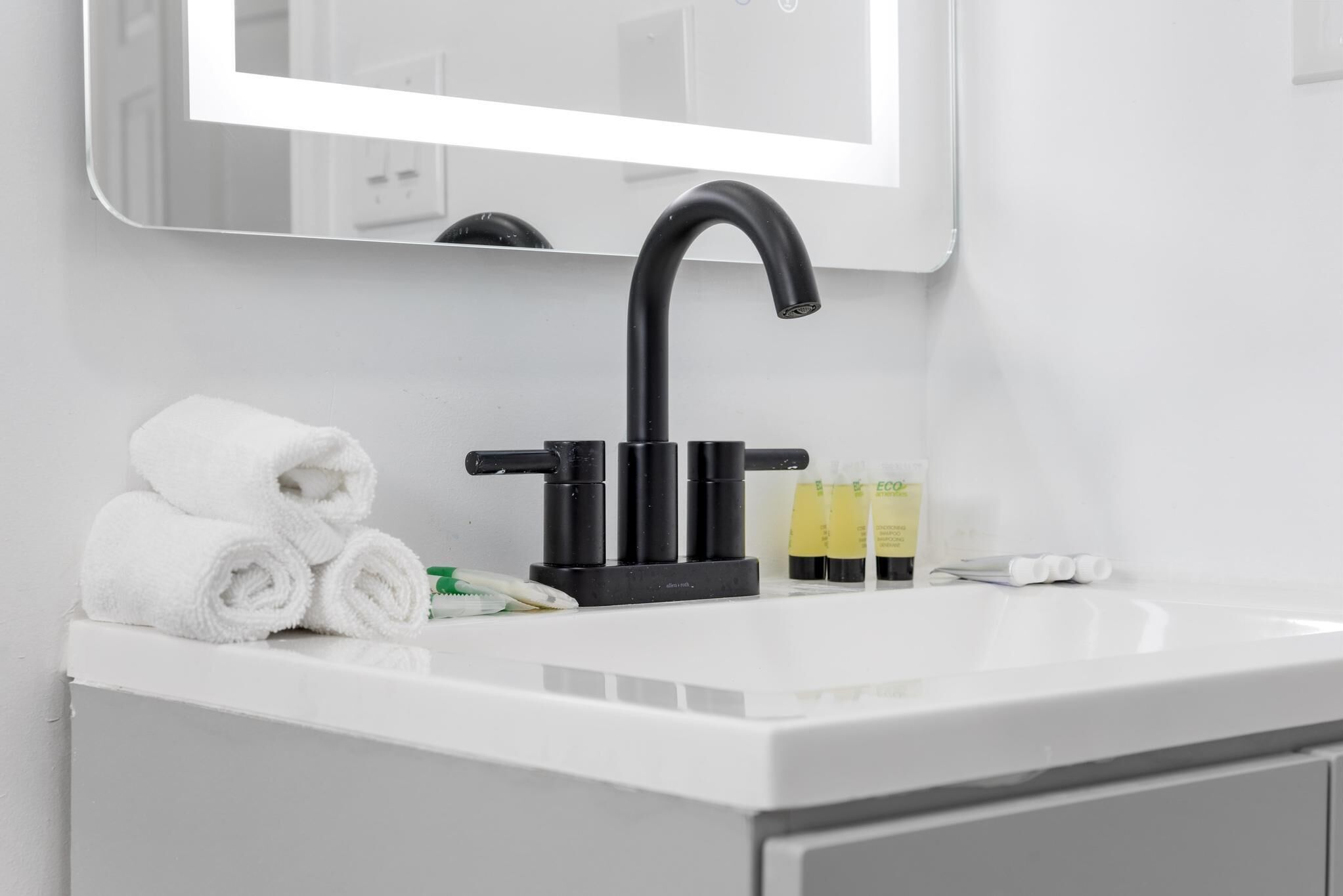A white bathroom sink with a black faucet, a mirror above it, and toiletries including a toothbrush, toothpaste, and a towel.