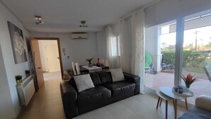 Uma sala de estar moderna com um sofá de couro preto, uma área de jantar com mesa e cadeiras, e uma grande porta de vidro deslizante que dá para um pátio externo.