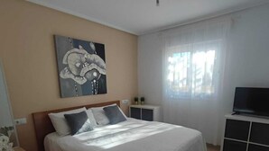 Um quarto com cama, ventilador de teto, janela com cortinas e um quadro na parede.