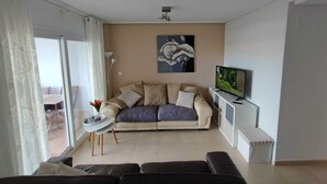 Uma sala de estar moderna com sofá, mesa de centro, TV e porta de vidro deslizante para área externa.