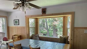 A dining area with a table and chairs, a ceiling fan, and large windows with a view of trees.