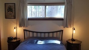 A bedroom with a bed, two bedside lamps, a window with curtains, and a framed picture on the wall.