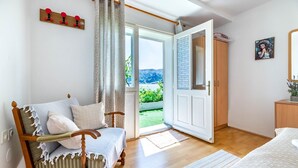 Une chambre à coucher avec un lit en bois, une chaise en bois, un bureau et une porte donnant sur un balcon.