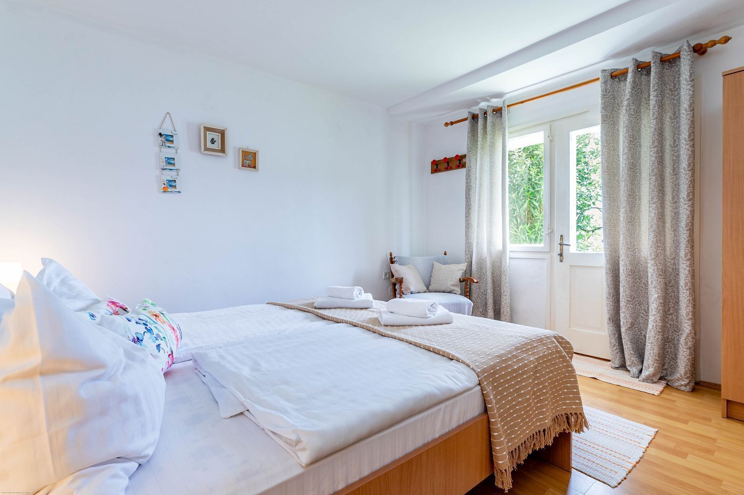 Een slaapkamer met een bed, een houten garderobe, een raam met gordijnen en een klein wandplankje met foto's.