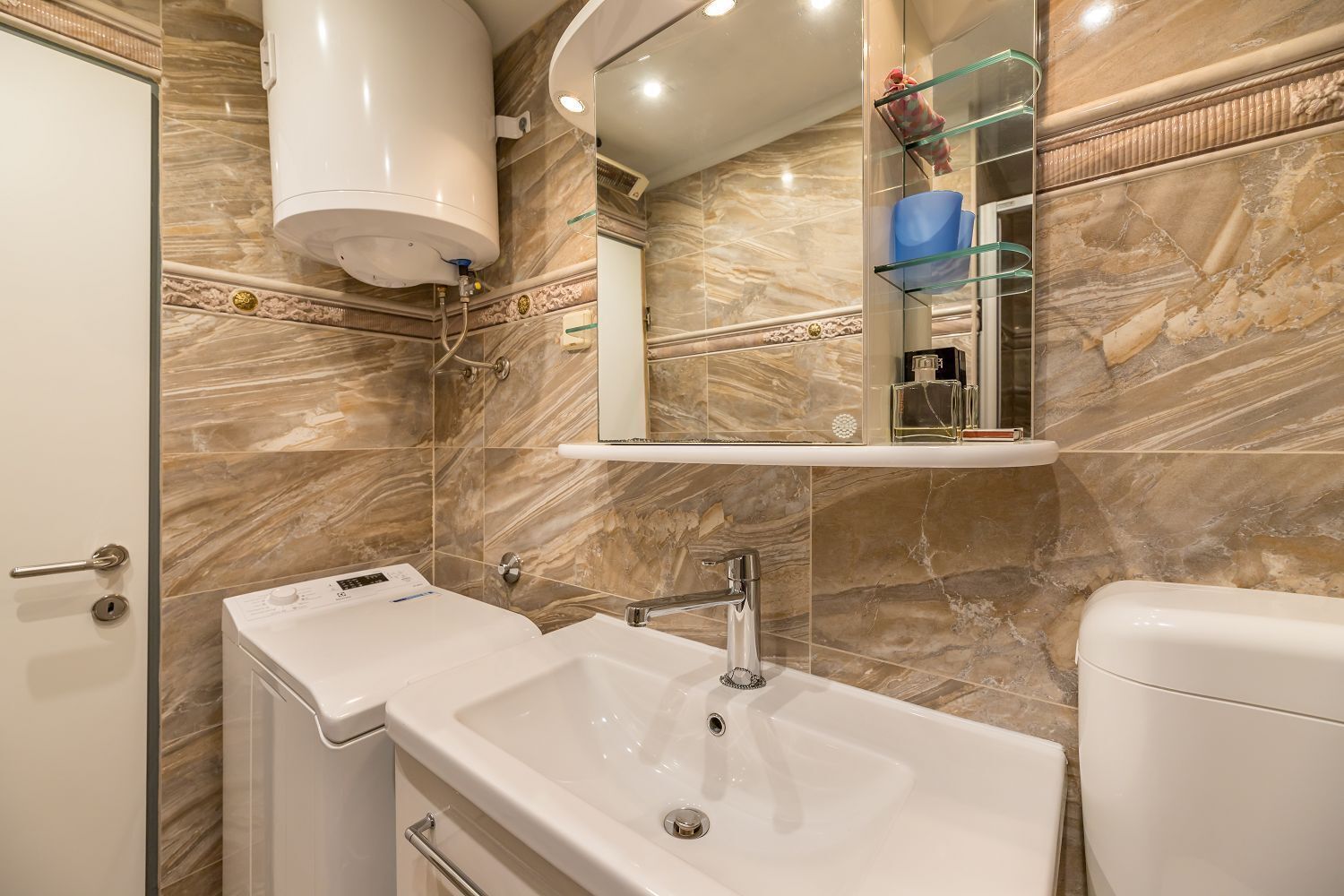 Une salle de bain avec un mur en marbre, un lavabo, un miroir et des toilettes.