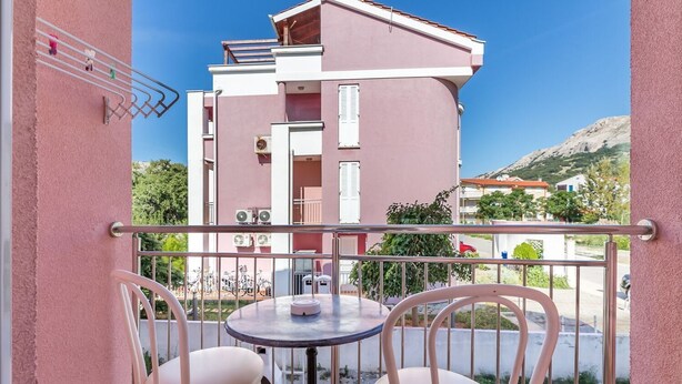 A balcony with two white chairs and a small round table, overlooking a pink building with balconies and air conditioning units. - With air conditioning, WiFi, balcony only 350 metres to the beach (Baska)