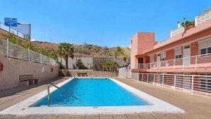 Una piscina con solárium de azulejos, un banco y un edificio con balcón al fondo.