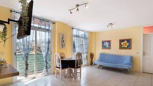 Un amplio salón con una mesa de comedor y sillas, un sofá, y ventanas grandes con cortinas.