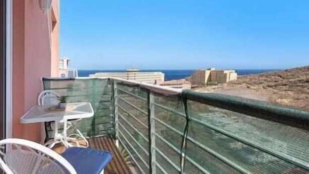 Un balcón con mesa y sillas, con vistas a un litoral rocoso y al mar.