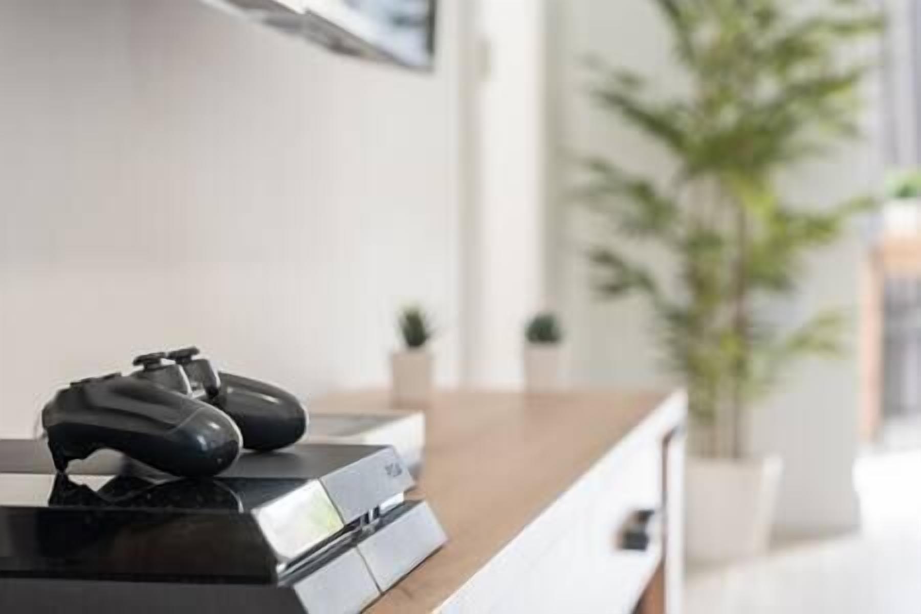 Une console de jeux avec une manette posée sur une surface en bois, probablement dans un salon ou un espace de divertissement.