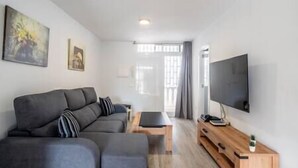 Un salon moderne avec un canapé d’angle gris, une table basse en bois et un téléviseur à écran plat fixé au mur.