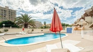 Une piscine avec des chaises longues blanches et un parasol rouge.