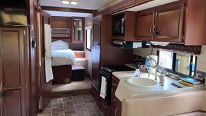 Interior compacto de una caravana con kitchenette, un dormitorio pequeño y un baño.