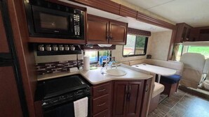 Cocina compacta para vehículo recreacional, con microondas, estufa, lavaplatos y armarios.
